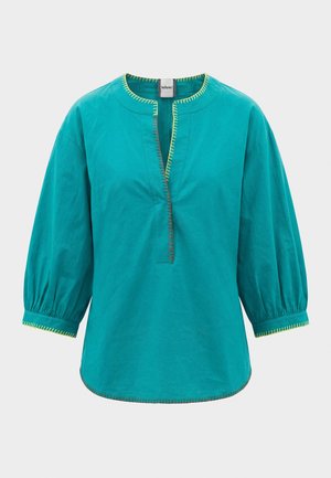 Tyrkysová halenka s tříčtvrtečními nafouknutými rukávy, kulatým výstřihem, žlutým kontrastním švem a předním rozparkem.