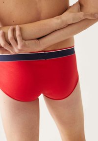 Boxer-briefs pour hommes rouges avec une coupe ajustée, présentant une taille bleu marine avec des rayures blanches. Le matériau semble lisse et élastique.