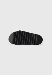 Black shoe sole with deep horizontal grooves for traction, isolated on a gray background.