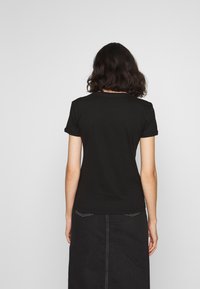 Camiseta de algodón negra con mangas cortas, escote redondo y una textura suave. La parte trasera muestra detalles de costura y un diseño ajustado.