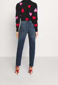 Suéter negro con patrones de corazones rosas y rojos, combinado con jeans de mezclilla azules y sandalias rojas de tacón alto. Mangas largas y silueta ajustada.