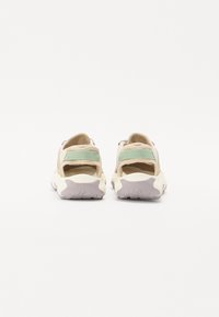 Sport sandals featuring a beige upper with green straps, open back, and textured white sole with gray accents for enhanced grip.