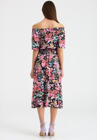 Robe fleurie à épaules dénudées avec manches courtes, présentant des motifs roses, verts et noirs. Comprend une taille smockée et un ourlet mi-long.