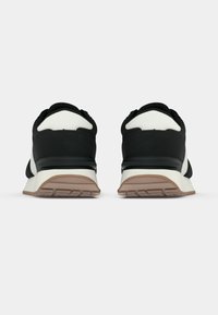 Μαύρα αθλητικά παπούτσια με λευκές λεπτομέρειες, στρογγυλεμένη γραμμή, υφασμάτινο επάνω μέρος με υφή και ταμπά καουτσούκ σόλα με σχέδια πέλματος.