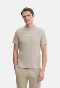 Camiseta de color beige claro con cuello redondo y mangas cortas, que presenta un sutil logo de Calvin Klein en un tono más claro en el pecho.