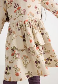 Floral-patterned dress in beige cotton with ruffled tiers; features multicolored flowers, green leaves, and a soft texture.