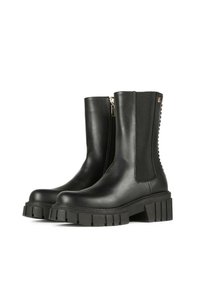 Botas de tobillo de cuero negro con una suela gruesa y estriada, paneles elásticos en los laterales, cremallera lateral y tachuelas decorativas en la parte trasera.