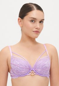 Cveče vijolične čipkaste bralette z trigonalnimi skodelicami, ki vsebujejo zapletene cvetlične vzorce, nastavljive naramnice in zlat odtenek krožne dekoracije na sredini.