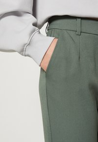 Grijze sweatshirt met geribbelde manchetten, gecombineerd met groene op maat gemaakte broeken met een zijzak en een soepel, gestroomlijnd uiterlijk.