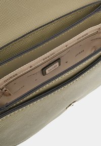 Interno di una borsa a tracolla di un verde oliva chiaro con texture, composto da due scomparti, foderato in beige con un motivo sottile e una tasca con zip.