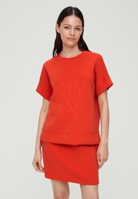 Rode sweatvest en rok set gemaakt van zachte stof; beschikt over een gelaagd ontwerp, korte mouwen en een subtiel bladpatroon dat op de voorkant is gedrukt.