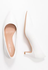 Pump bianco con tacco alto, punta appuntita, texture liscia e design leggermente curvato. Presenta una soletta beige e un tacco piccolo.