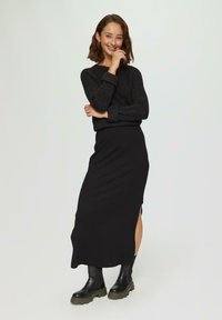 Zwarte geribbelde trui met lange mouwen, gecombineerd met een zwarte midi rok met een zijsplit. Draag het met stevige zwarte laarzen.