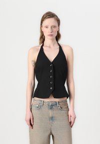 Svart halterneck topp med V-hals, tettsittende liv og seks knapper foran. Kombinert med lyseblå, lett falmede jeans.