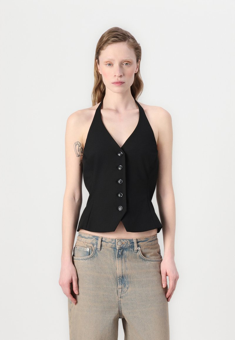 Svart halterneck topp med V-hals, tettsittende liv og seks knapper foran. Kombinert med lyseblå, lett falmede jeans.