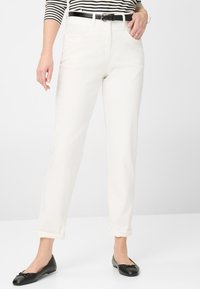 Hvide straight-leg jeans med opfoldet kant, featuring en frontknap og lynlås i lukning, parret med sorte balletflader og en stribet top.