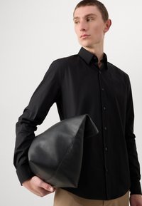 Zwarte overhemden met lange mouwen, gladde textuur, met kraagontwerp. Het model houdt een zwarte leren driehoekige tas vast met een zachte afwerking.
