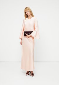 Μακρύ, εφαρμοστό φόρεμα σε απαλό ροζ σατέν με μανίκια καμπάνα. Συνδυασμένο με σκούρο τσαντάκι με ασημένες λεπτομέρειες και ψηλοτάκουνα σανδάλια.