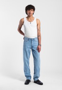 Jeans di denim azzurro chiaro con una vestibilità comoda, dotati di chiusura a bottone e passanti per la cintura, abbinati a una canotta bianca a costine.
