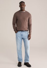 Pull marron à col rond, jean bleu clair, ceinture noire et chaussures marron foncé. Design simple avec une texture lisse et une coupe décontractée.