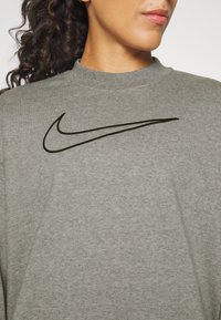 Šedá mikina s měkkou texturou a kulatým výstřihem. Na hrudi je výrazné černé logo Nike swoosh.