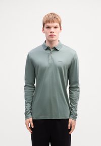 Long-sleeve polo shirt in soft, muted green fabric. Features a three-button placket, subtle logo, and a relaxed fit. Plain design, no patterns.