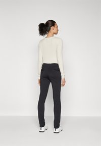 Top a maniche lunghe di un beige chiaro abbinato a pantaloni neri aderenti con vita bassa e tasche laterali con zip, indossato con scarpe da ginnastica bianche.