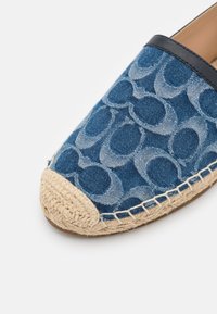 Denim espadrille-sko med ett blått och vitt cirkulärt mönster, beige flätad jute-detalj vid tån och en mörk läderkant.