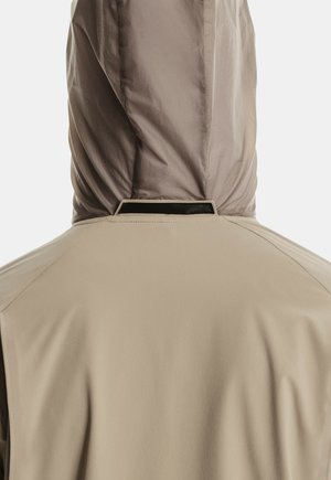 Giacca beige con cappuccio vista dal retro, che mostra la texture del tessuto e i dettagli delle cuciture attorno al colletto e al cappuccio.