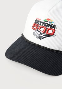 Λευκό και μαύρο τζιν καπέλο με κεντημένο λογότυπο "38th Daytona 500" και πολύχρωμες αγωνιστικές σημαίες στην μπροστινή πλευρά.