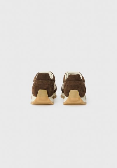 Braune Wildleder-Sneaker mit einer cremefarbenen Ferse und weißer Zunge. Gummisohlen mit strukturiertem Muster für guten Halt.