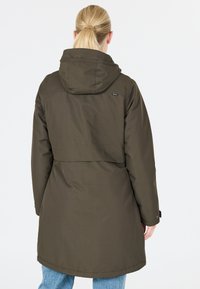 Olijfgroene waterdichte jas met capuchon, zichtbare stiksels en geplooid detail aan de achterkant, gecombineerd met lichtblauwe jeans.