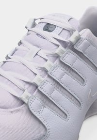 Κλείσιμο λήψης λευκού αθλητικού παπουτσιού με πλεκτό ύφασμα, συνθετικές επικαλύψεις, μοναδικό σύστημα δεσίματος και μικρό λογότυπο μάρκας στη γλώσσα και στο πλάι.