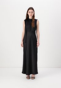 Black sleeveless maxi dress with soft, silky texture, gathered waist detail, and a flowing silhouette. Paired with black strappy sandals.