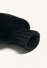 Brățară tricotată neagră cu o căptușeală moale din blană. Textura este netedă, având detalii tricotate în formă de coajă și o deschidere rotundă pentru o fixare strânsă.