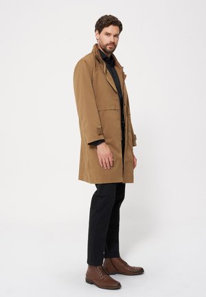 Brown waterproof coat with a high collar, button closure, and pockets, paired with black pants and brown lace-up boots.