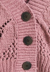 Stickad kofta i mjuk rosa med ett strukturerat mönster. Har fyra mörka knappar fram och en ribbad krage.