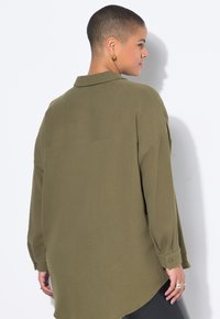 Chemise verte olive, texturée, avec col, manches longues et poignets boutonnés. Ourlet arrière plus long, coupe décontractée, design minimaliste.