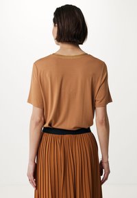 Blusa marrón de manga corta y cuello redondo con detalles dorados, combinada con una falda marrón plisada con una cinturilla elástica negra.