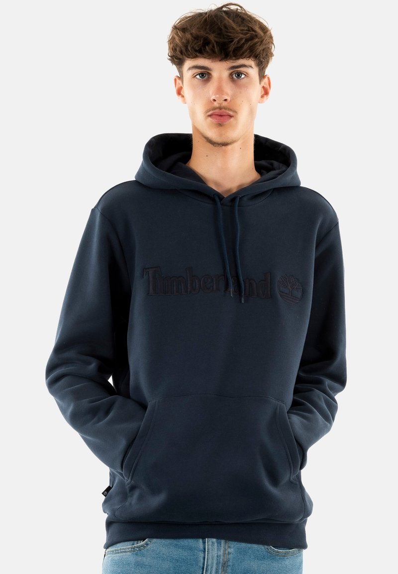 Navy blauwe hoodie van zacht materiaal met een kangoeroezak, verstelbare trekkoordcapuchon en reliëf "Timberland" logo op de borst.
