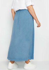Gonna maxi in morbido tessuto blu chiaro con vita elastica e silhouette dritta. Abbinata a sneakers bianche per un contrasto.