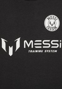 Camiseta negra de algodón con gráficos impresos en blanco, que incluyen un logo y el texto "SISTEMA DE ENTRENAMIENTO MESSI". Diseño simple y moderno.