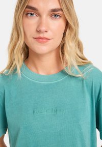 T-shirt in cotone turchese con scollo a giro e logo ricamato "Quiksilver". Maniche corte e texture liscia.
