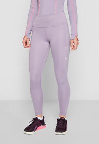 Šviesiai violetinės legging'ų kelnės su aukštu juosmeniu, lygiu paviršiumi ir diskretiška šonine kišene. Suderinta su juodais ir rožiniais sportiniais bateliais.