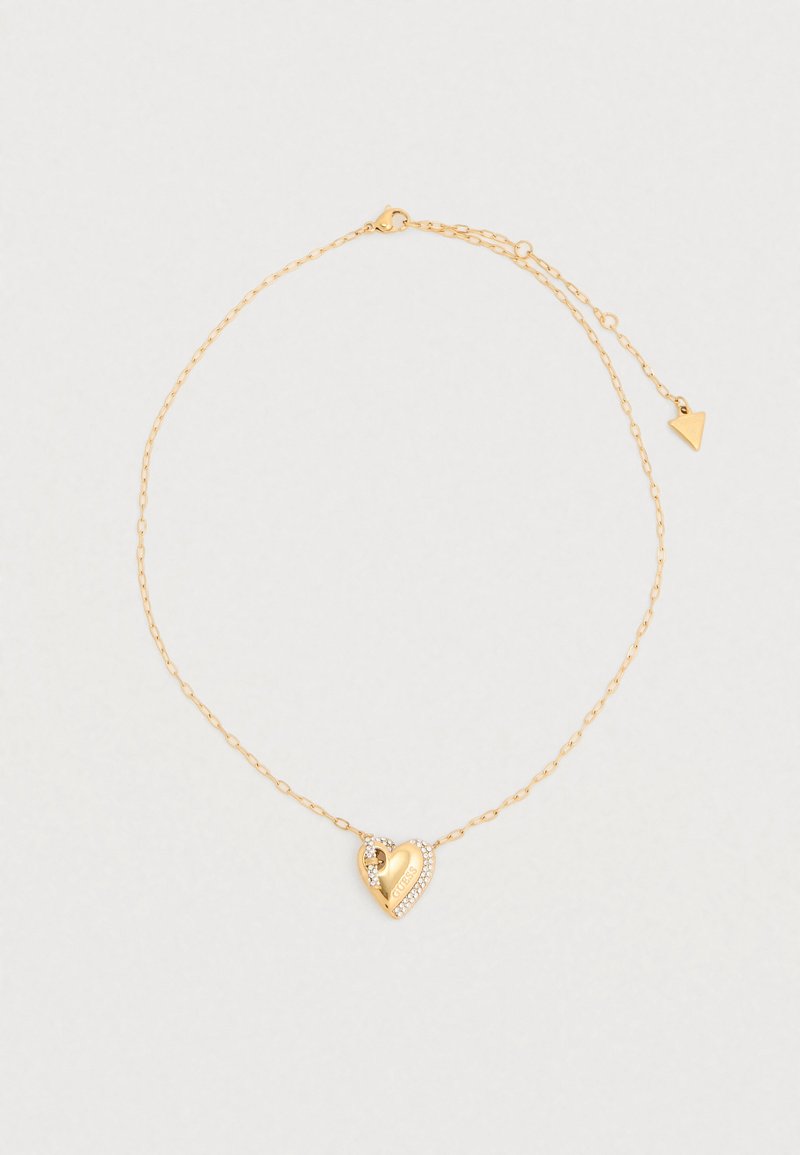 Κολιέ σε χρυσό τόνο με μενταγιόν σε σχήμα καρδιάς, διακοσμημένο με ένα μικρό κρύσταλλο και χαραγμένη επωνυμία, προσαρτημένο σε μια λεπτή αλυσίδα.