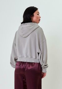 Grijze hoodie met capuchon, geribbelde manchetten en onderrand. Draagt prettig met glanzende bordeauxrode broek. Gestyled met een relaxte pasvorm en een zachte textuur.