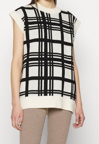 Haut sans manches en maille crème à motif tartan noir, doté d'un col rond et d'un ourlet côtelé. Tissu texturé avec une coupe décontractée.