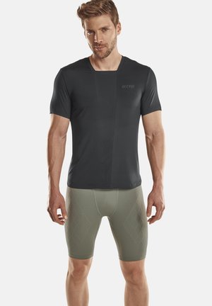 Schwarzes kurzärmliges Sportshirt mit einem strukturierten Design, kombiniert mit hellolivenen Kompressionsshorts mit einem Rautenmuster.