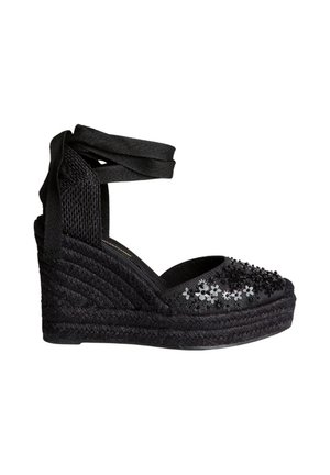 Sandalia negra de cuña con lazo para atar en el tobillo, adornos florales de cuentas en el dedo y suela plataforma trenzada de cuerda.