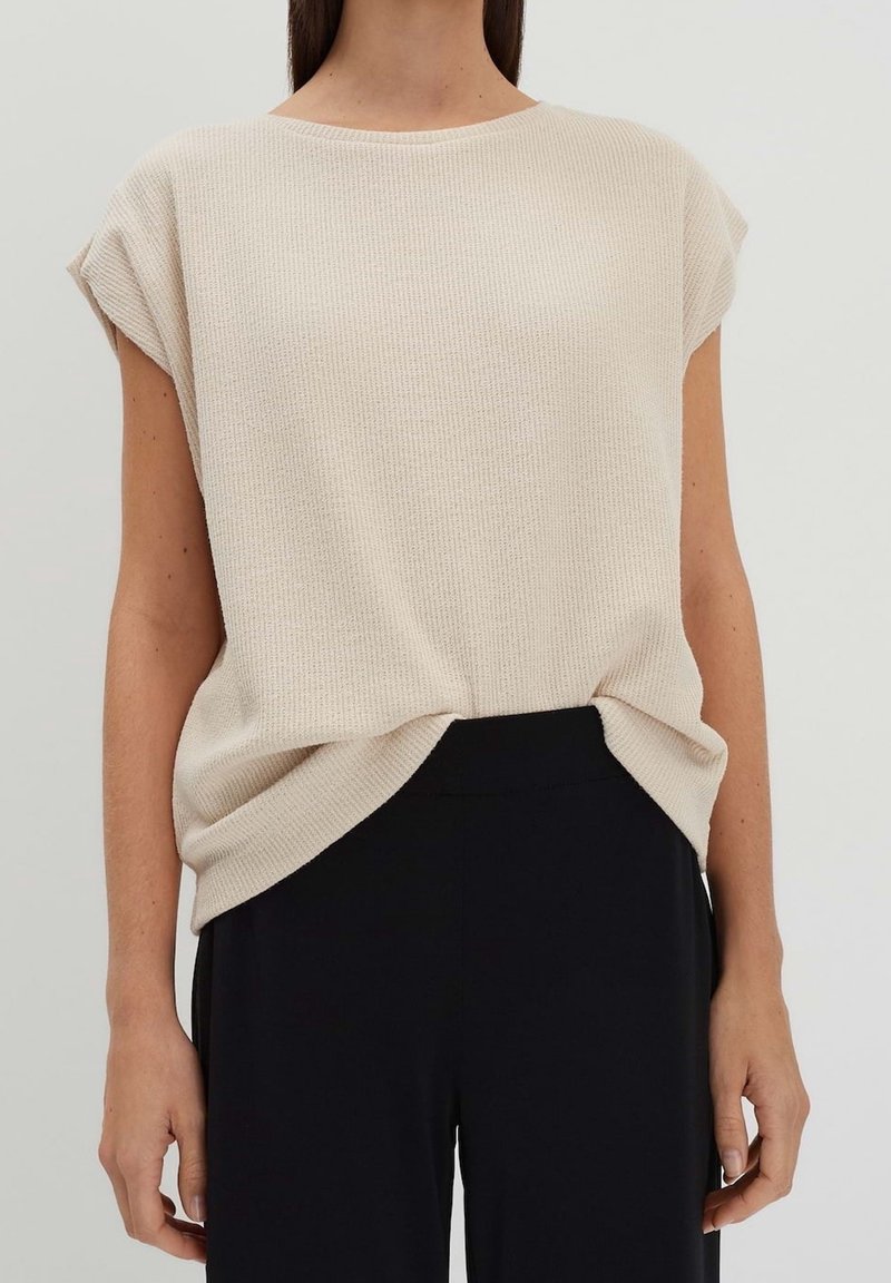 Beige, ribbat stickad t-shirt med lös passform, korta ärmar och rundad halsringning, kombinerad med svarta byxor och knuten framtill.